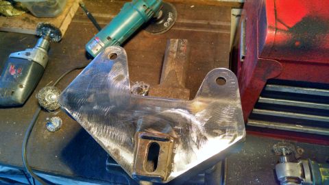 1992 Ford Bronco - A metal bracket is being worked on with various tools including a drill with a wire brush attachment and an angle grinder. The bracket appe…