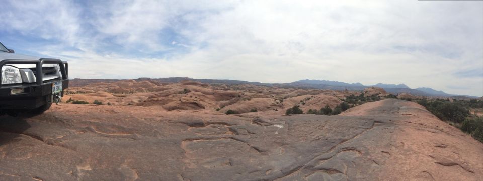 Silver SUV with bull bar and winch parked on rocky terrain, panoramic desert landscape.