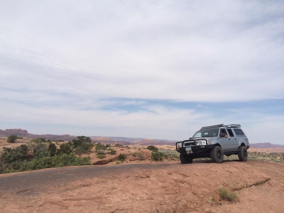 Silver Nissan Frontier pickup truck with off-road modifications in a desert landscape.