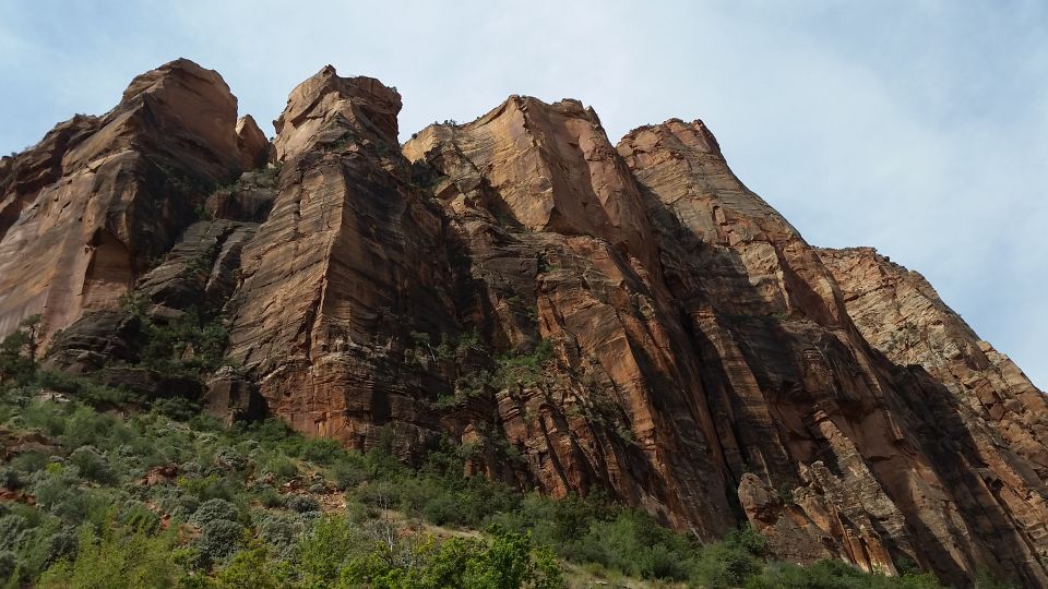 Towering sandstone cliffs with layered red and brown rock formations and green vegetation at the base.