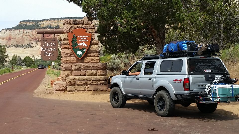 Silver Nissan Frontier pickup truck at Zion National Park entrance with camping gear.