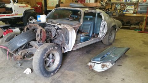 Classic American muscle car coupe in a garage, disassembled with front end removed.