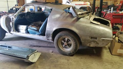 2015 Chevrolet new - A bare metal, partially disassembled classic car is parked in a garage. The driver's side door is open, revealing the blue interior and sea…