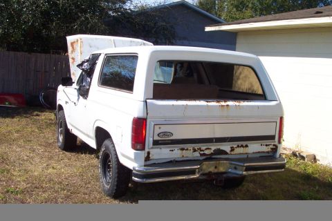 1985 Ford Bronco - This older model Ford Bronco is seen in a grassy area with a fence and building in the background.