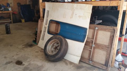 2015 Chevrolet new - A white car hood with a blue insert and a tire are leaning against a wooden structure in a garage. A wooden folding table is also visible.