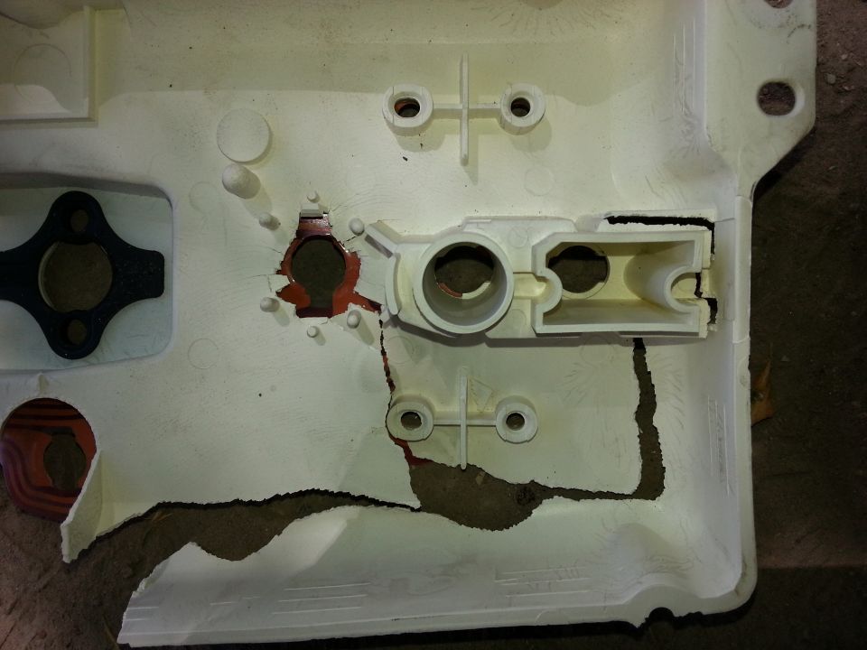 Cracked white plastic vehicle panel with broken mounting bosses and red gasket showing through fractures