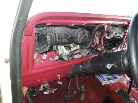 1978 Ford Bronco - The interior of a vehicle's dashboard is shown with the center console removed, revealing air ducts and wiring. The red dashboard trim and…