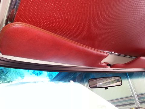 1978 Ford Bronco - The interior of a vintage vehicle's headliner and sun visor are visible in red, with a rearview mirror mounted to the windshield.