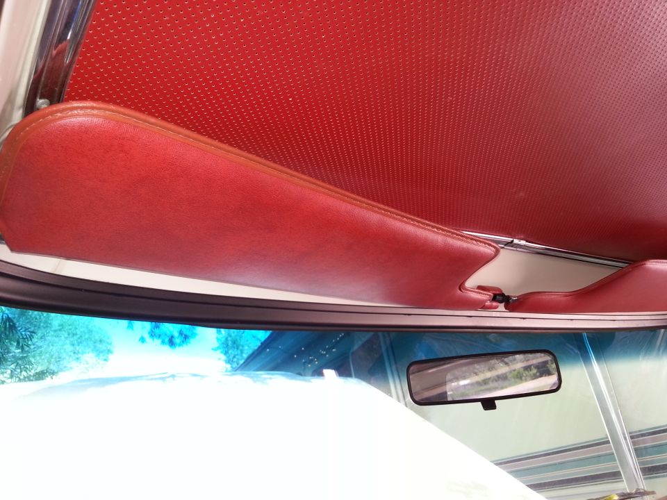 Red perforated headliner and red padded sun visor in a vintage vehicle interior.