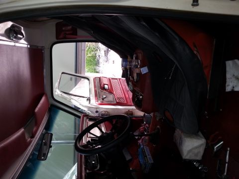 1978 Ford Bronco - Interior view of a classic vehicle, likely a 1978 Ford Bronco, showing red vinyl seats, a steering wheel, and a partially open driver's sid…