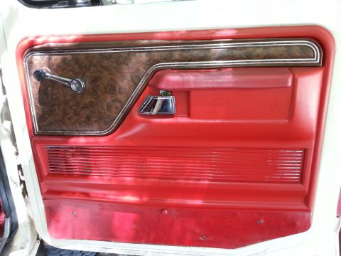 1978 Ford Bronco - The interior door panel of a classic vehicle features a wood-grain accent panel with a chrome window crank and a red vinyl armrest and lowe…