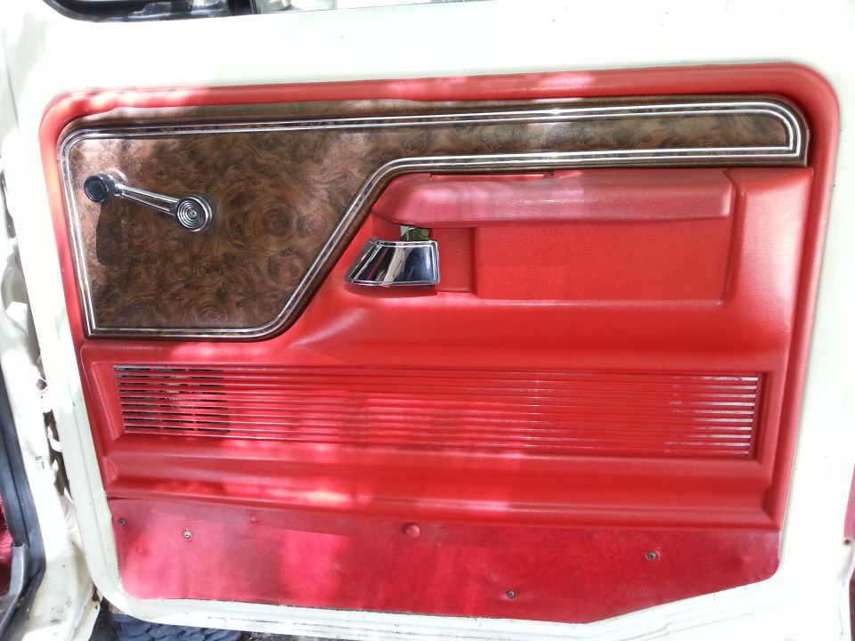 Classic vehicle red interior door panel with wood grain accent, chrome window crank, and speaker grille.
