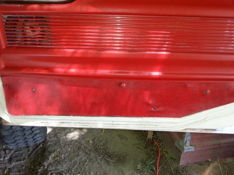1978 Ford Bronco - A close-up interior view of a red and off-white door panel, likely from a vintage Ford Bronco, showing a speaker grille and textured vinyl…