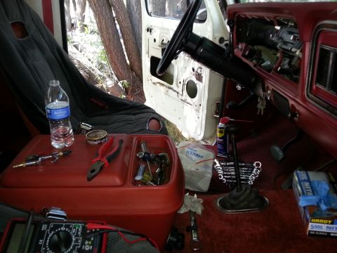 1978 Ford Bronco - The interior of a vintage Ford Bronco shows a red plastic storage bin filled with tools, a bottle of drinking water, and a can of Copenhage…