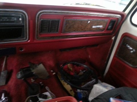 1978 Ford Bronco - The interior of a vintage Ford Bronco is shown, featuring a red dashboard with wood grain accents and a floor-mounted gear shifter. Various…