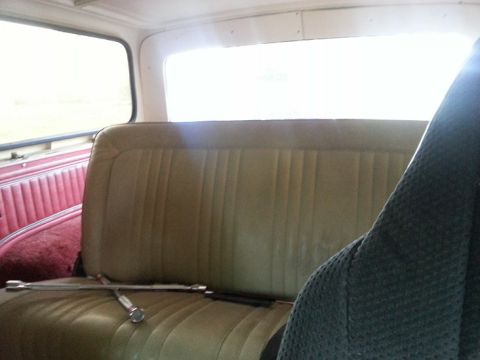 1978 Ford Bronco - The interior of a vehicle shows a bench seat with a lug wrench resting on it. The side paneling is red and the seat is a light brown color.