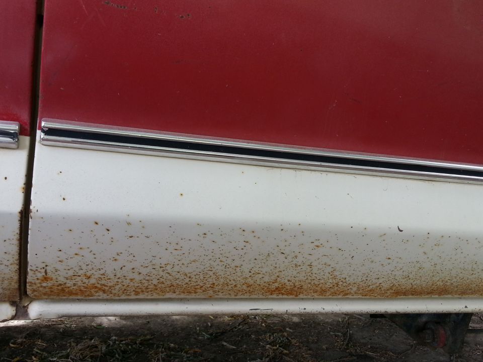 Close-up of a red and white vehicle panel with significant rust on the white lower section.