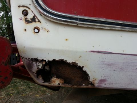 1978 Ford Bronco - A close-up view of significant rust damage on the lower rear quarter panel of a vintage vehicle, likely a 1978 Ford Bronco. The white paint…