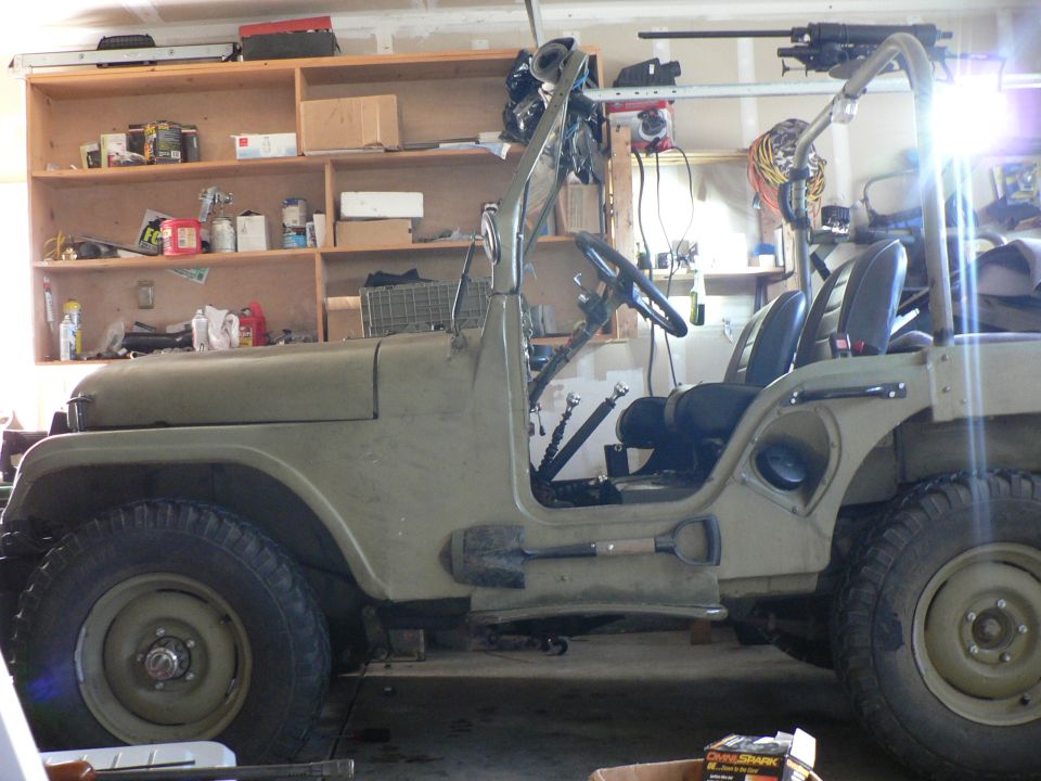 Olive drab 1952 Jeep CJ5 parked in a garage, side view.