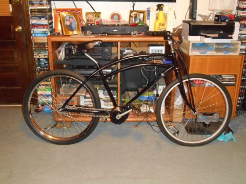 Black cruiser bicycle with chrome spokes and sprung saddle, parked indoors.