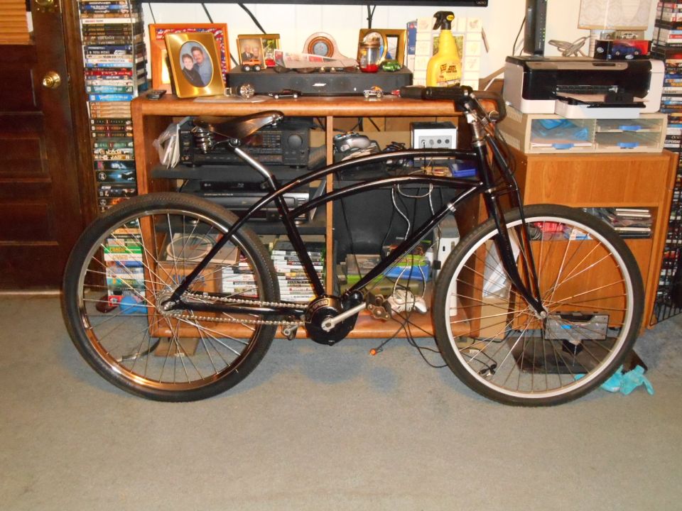 Black cruiser bicycle with chrome spokes and sprung saddle, parked indoors.