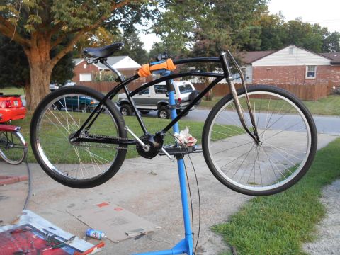 Black bicycle on a repair stand, with a red Ford Mustang and houses in the background.