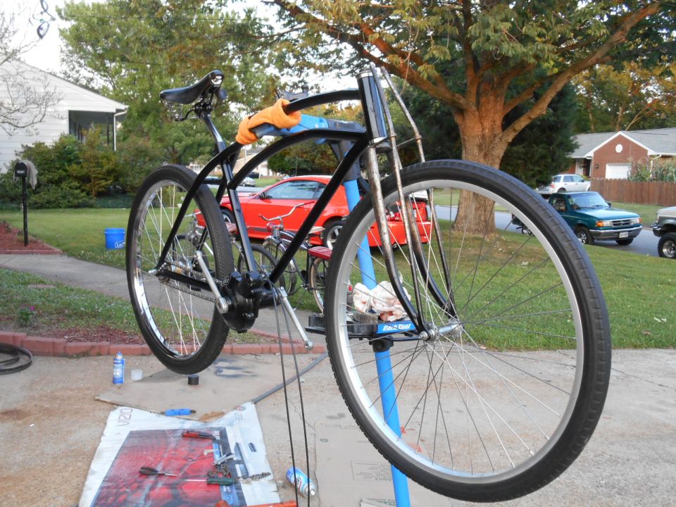 Black bicycle on repair stand, red car and green pickup truck in background.