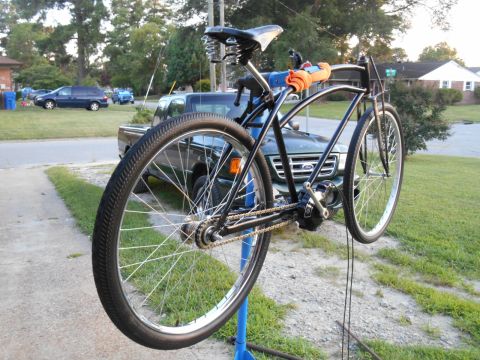 Black bicycle with motor on repair stand, orange grips, residential background.