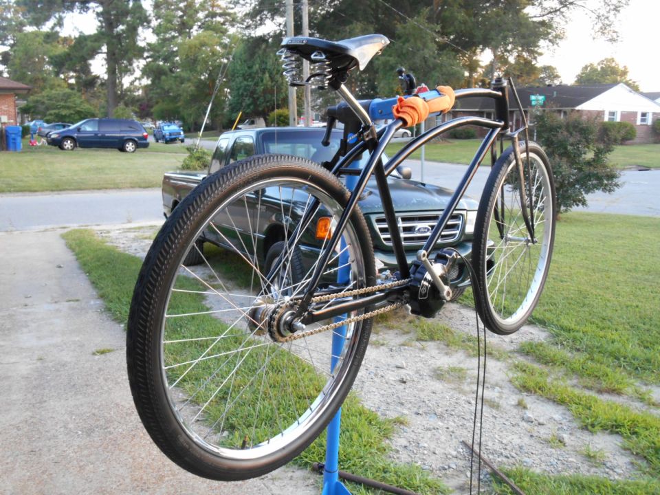 Black bicycle with motor on repair stand, orange grips, residential background.