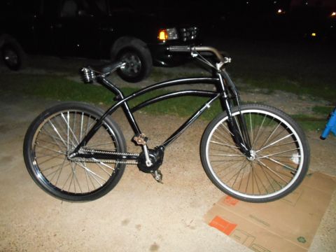 Black cruiser bicycle with chrome handlebars and spokes, parked on concrete.