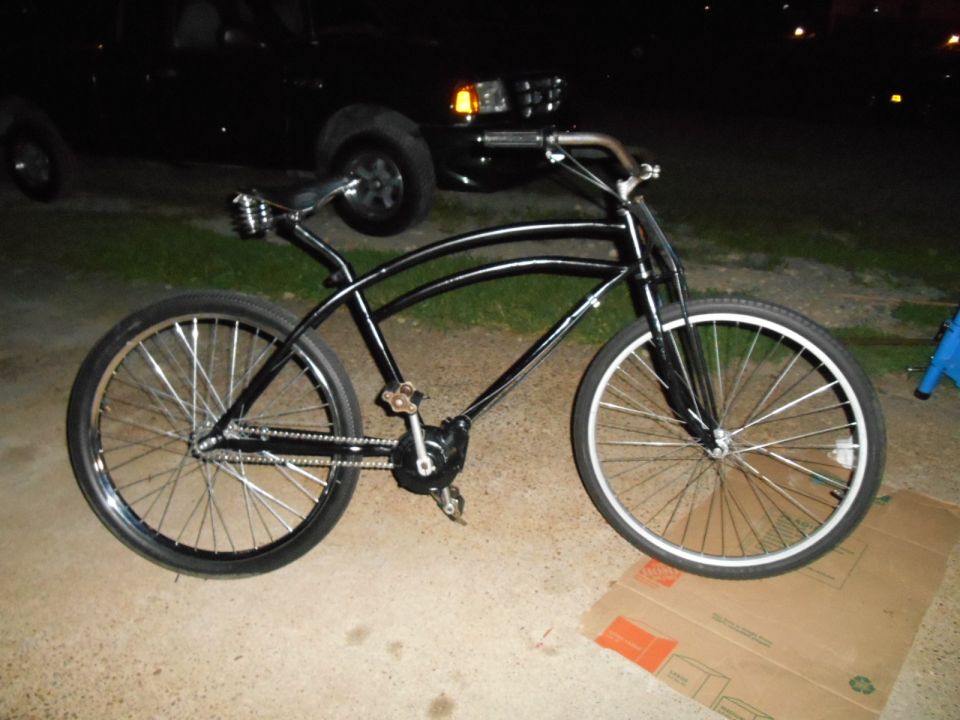 Black cruiser bicycle with chrome handlebars and spokes, parked on concrete.