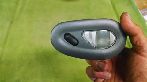 1992 Ford Bronco - A hand holds a gray overhead interior light assembly with a black button and a clear lens. The assembly appears to be from a vehicle.