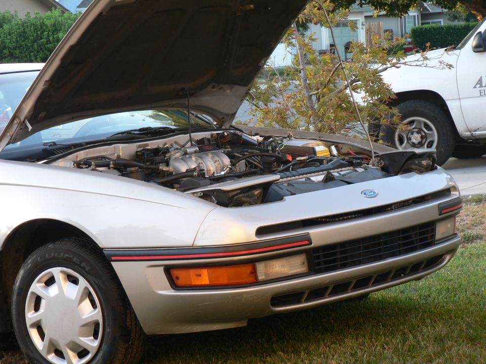 Silver 1991 Ford Probe with hood open, showing engine. White pickup truck in background.