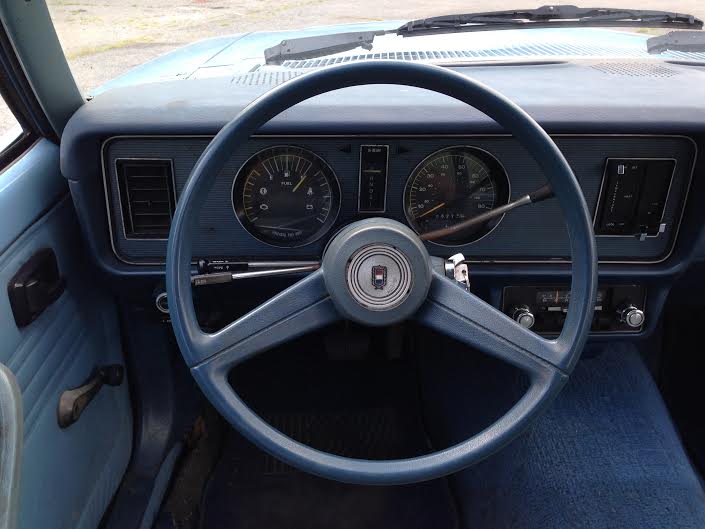 Vintage car dashboard with blue steering wheel, gauges, and radio.