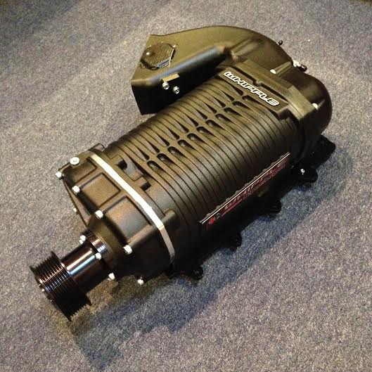Black Whipple supercharger with ribbed casing and front pulley system on gray carpet.