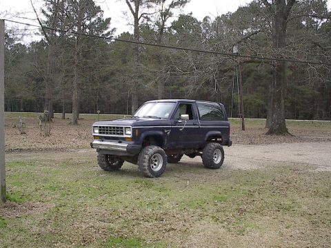 1985 Ford Bronco II - Lifted 1985 Ford Bronco II with aftermarket wheels and tires sits in a grassy area.