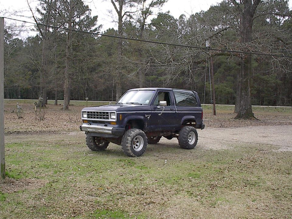 Dark blue lifted two-door Ford Bronco II SUV on large tires parked outdoors