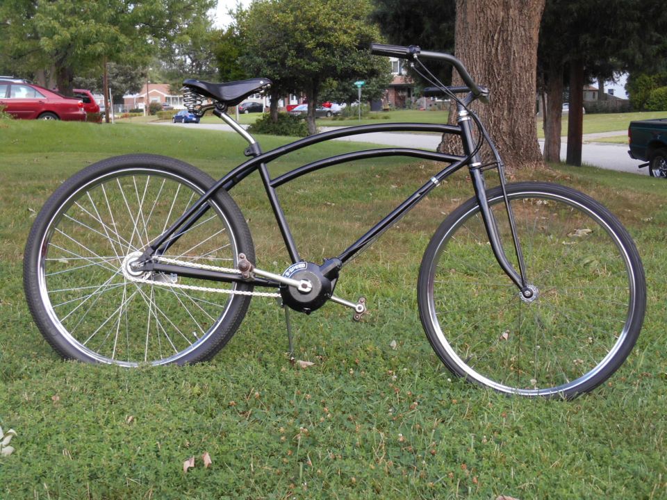 Black cruiser bicycle with wide handlebars and a single chainring, parked on grass