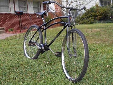 black cruiser bicycle with curved frame and chrome rims parked on grass in front of a brick house