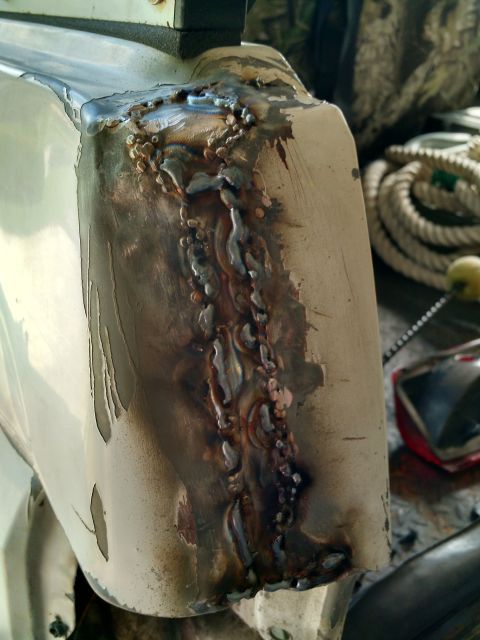 1992 Ford Bronco - This close-up shows significant body damage and crude welding repairs on a vehicle panel, with a rope and camouflage material in the backgr…