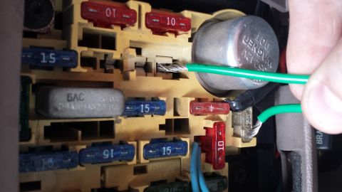 1995 Ford Bronco - A hand is shown connecting a green wire to a fuse in a vehicle's fuse box.