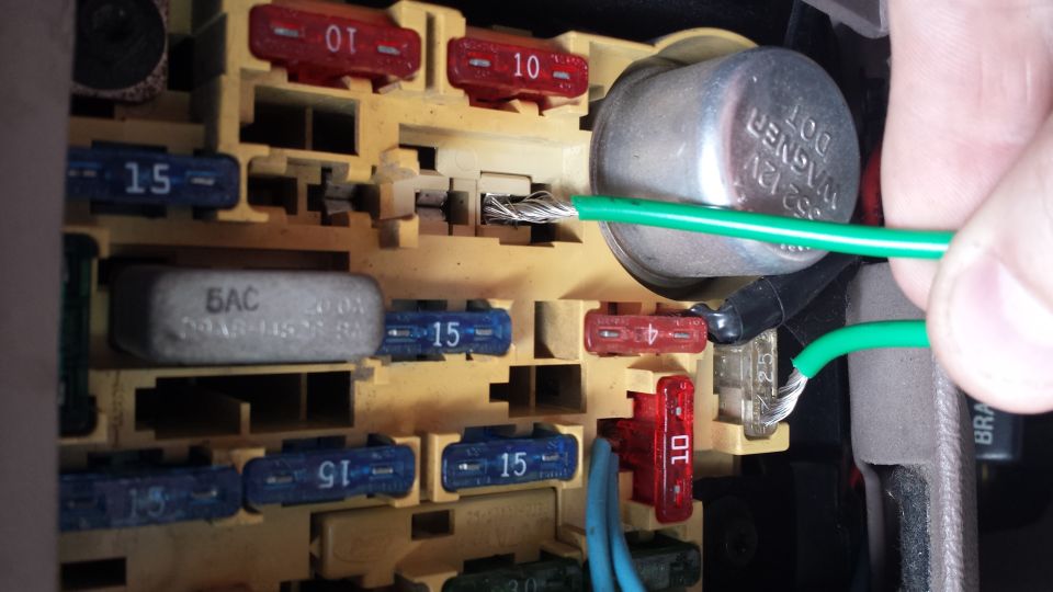 close-up of a car's fuse box with a hand inserting a green wire