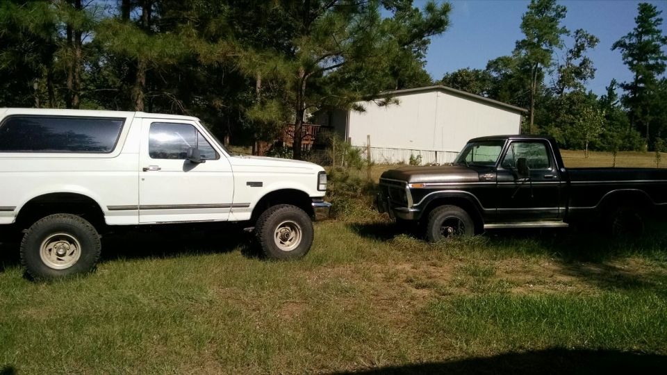 White 1996 Ford Bronco parked next to a brown Ford pickup truck