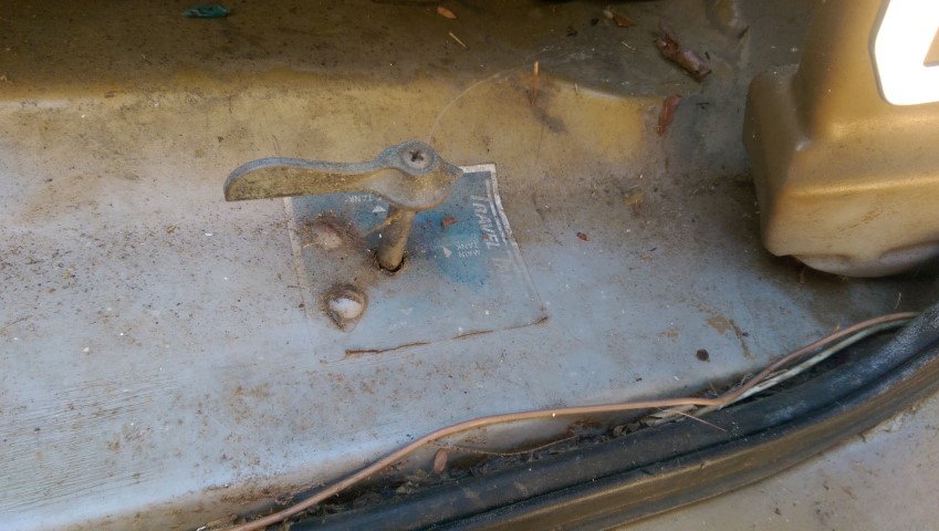 Close-up of a rusty door latch and a small blue sticker with text on a vehicle's interior panel
