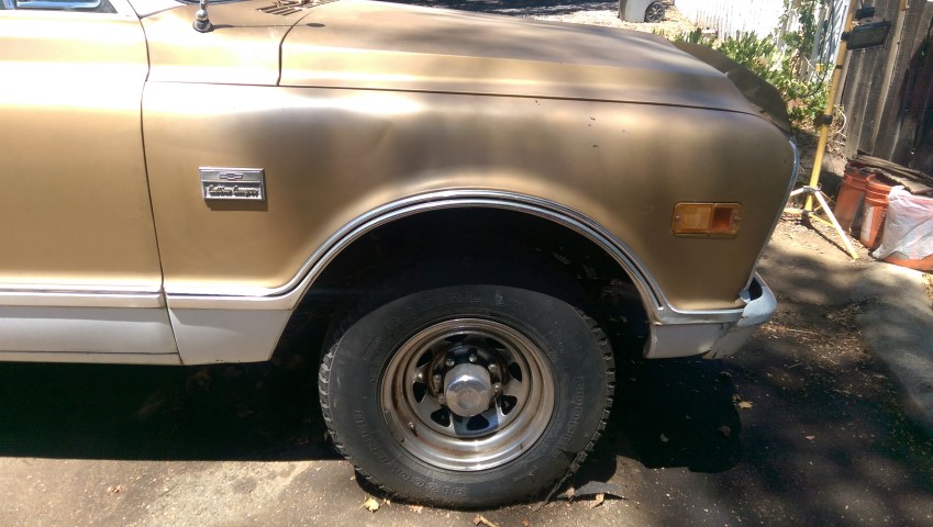 Gold and white pickup truck fender and wheel. Badge reads 'Custom Camper'