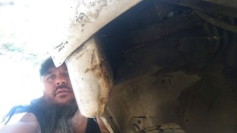 1968 Chevrolet C/K Pickup - Man inspecting the underside of a vehicle, focusing on a corroded wheel well area.