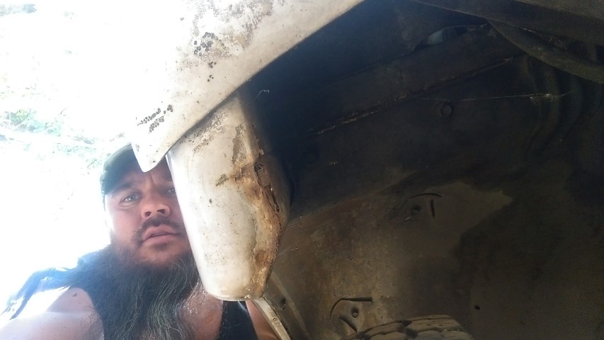 Man peers into a rusted wheel well of a vehicle