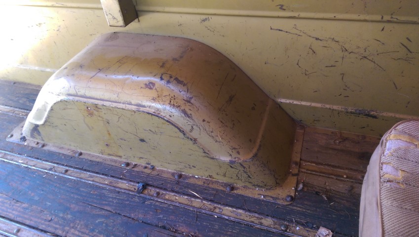 Interior shot of a truck bed showing the wheel well and wooden floor. A bit of the seat is visible