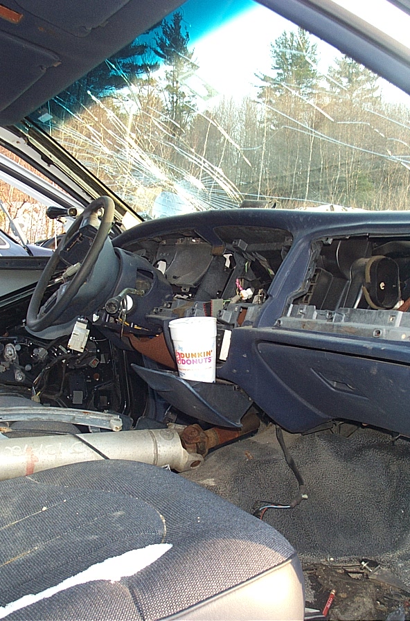Interior of a car with a cracked windshield, missing dashboard parts, and a Dunkin' Donuts cup