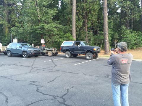 1946 Jeep CJ5 - A man takes a photo of a Ford Bronco and a vintage Jeep trailer in a parking lot.